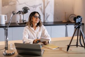 Infoprodutora grava uma aula online com câmera e laptop