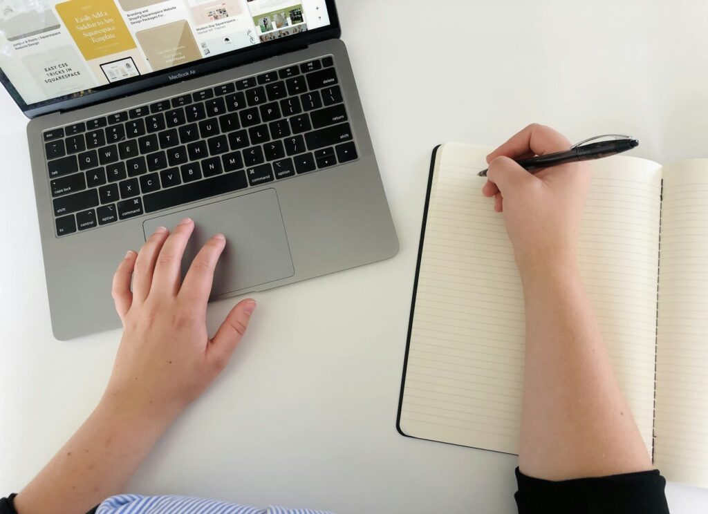 Pessoa registra ideias em caderno ao lado de notebook durante processo criativo
